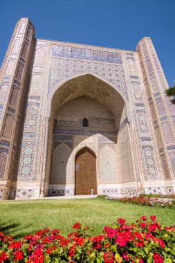 Ön planda bahçe ve çiçeklerle Bibi Khanum Camii 'nin kapısı görünüyor.