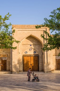 Bukhara, Uzbekistan - 08 July 2024: Woman with child on tricycle in Toqi Sarrofon neighborhood. clipart