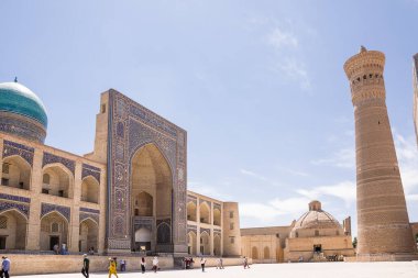 Buhara, Özbekistan - 09 Temmuz 2024: Buhara 'da turistlerin bulunduğu Madrassa, minare ve meydanın cephesi