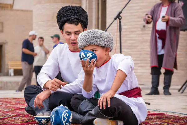 Khiva, Özbekistan - 11 Temmuz 2024: Geleneksel kılık değiştirmiş iki Özbek erkek çocuğu, geleneksel bir fincandan çay içiyorlar.
