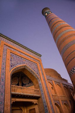 Gün batımında Khodja Minaresi ve portalının alçak açılı görüntüsü, sıcak ışık Özbekistan 'ın Khiva kentindeki tarihi mimariyi aydınlatıyor..