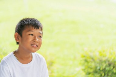 Beyaz tişörtlü şirin bir çocuğun portresi, şehir parkında oturup bulanık yeşil arka planı ve metin için coppy alanı ile düşünmektir..