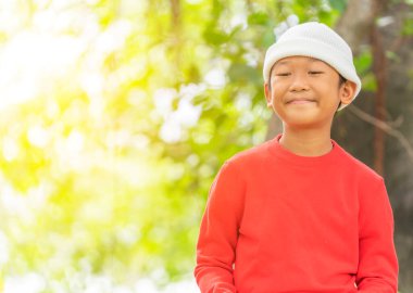 Kırmızı tişörtlü şirin çocuğun portresi şehir parkında bulanık yeşil arkaplan ve metin için coppy alanı ile duruyor..