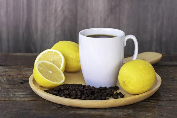 Lemon black coffee in white cup, coffee beans, lemon fruit, and lemon slices on wooden saucer and on vintage brown wooden background.