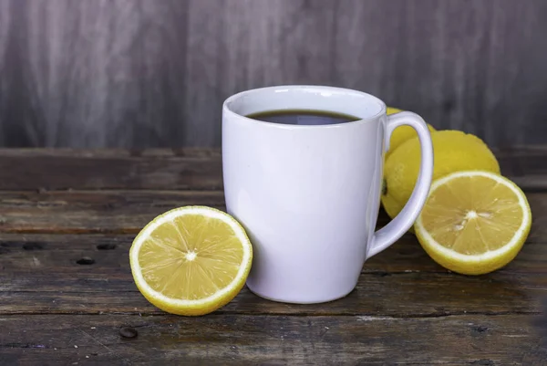 Black coffee lemon in white cup, lemon fruit, and lemon slices on vintage wooden background.