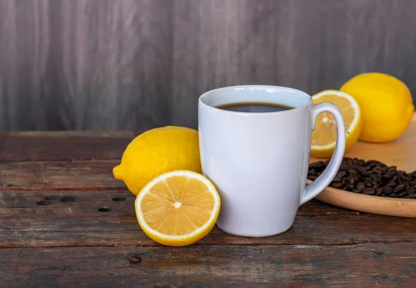 Lemon black coffee in white cup, coffee beans, lemon fruit, and lemon slices on wooden saucer and on vintage brown wooden background.