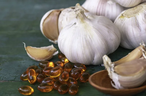 Garlic bulbs, capsules of oil extract, garlic cloves on wooden spoon, and on old green wooden background, Garlic can help reduce the risk of many diseases. Classified as healthy food