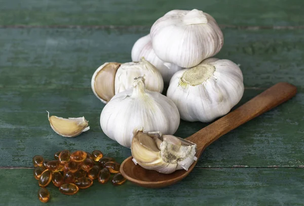 Garlic bulbs, capsules of oil extract, garlic cloves on wooden spoon, and on old green wooden background, Garlic can help reduce the risk of many diseases. Classified as healthy food.