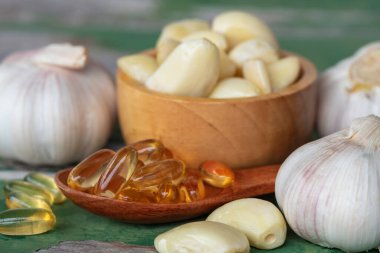 Altın sarımsak özlü yağ kapsülleri ahşap kaşıkta, sarımsak soğanları kahverengi kasede karanfil ve eski yeşil ahşap arka planda. Sarımsak birçok hastalığın riskini azaltmaya yardımcı olabilir. Sağlıklı yemek olarak sınıflandırılır..