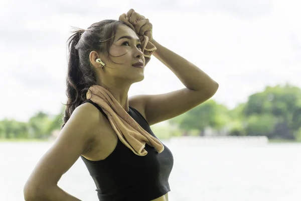 Portrait of young attractive fit woman wearing black sportswear with brown towel resting after workout sports exercises outdoors in background of park trees. Healthy lifestyle concept.