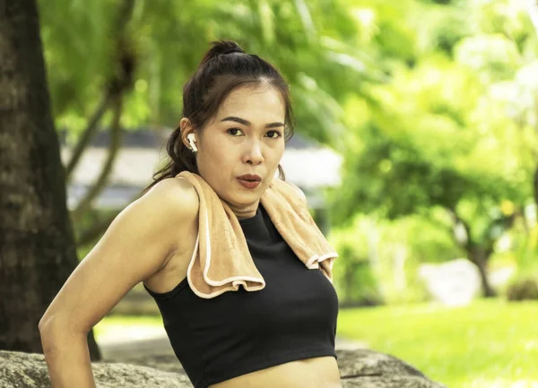 Portrait of young attractive fit woman wearing black sportswear with brown towel resting after workout sports exercises outdoors in background of park trees. Healthy lifestyle concept.