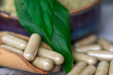 Paniklemenin ahşap kaşık içindeki bitkisel kapsülleri (Andrographis Paniculata) ve seramik kasede toz özü bulunan yeşil yapraklar eski ahşap arka planda..