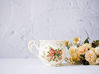 Antique cup of tea with saucer ,yellow orange rose flowers background ,porcelain vintage style ,old English coffee cup still life for wallpaper ,romance roses backgrounds 