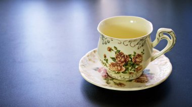 Koyu gri arka planda pembe gül porselen çay fincanı ile romantik çay saati afişi, boşluğu kopyala