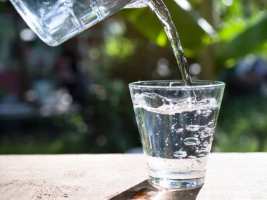 Mineral Saf Suyu Ahşap Masa 'ya, Işık Üzerindeki Masa' ya, Görünmez Yeşil Doğa Arka plan 'a, Kristal Cam' a Taze Buz Sıvısı İçeceğine, Diyet ve Sağlık İçin Arındırılmış Gıda 'ya döküyorum.