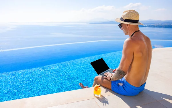 男人用笔记本电脑工作 而坐在无限大的游泳池边 海景秀丽 — 图库照片