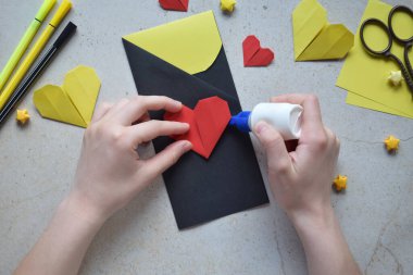 Handmade Crafting Process of a DIY Greeting Card with Origami Paper Hearts, Glue Application, Creative Stationery, Scissors, and Colorful Decorative Elements on a Light Artistic Background clipart