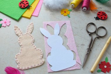 El yapımı Paskalya Tavşanı Keçeli Kalça Projesi Renkli İplikler, Makas, Kağıt Şablon ve Işık Arkaplanda Dekoratif Kalpler. Çocuklar ve Hobi Tutkuları İçin DIY Bahar Dekorasyonu Fikri