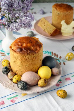 Renkli Yumurtalar ve Çiçekli Leylak Çiçekleri ile Lezzetli Paskalya Kulich. Geleneksel Bayram Pastası Bahar Elementleri ve Kutlama İçin Doğal Işık Sunar