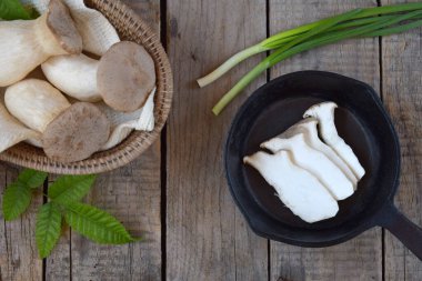 Dilimlenmiş kral istiridye mantarlarının taze otlar ve yeşil soğanlarla dolu siyah bir kasede üst görüntüsü. Yemek fotoğrafçılığı, organik mutfak görselleri ve sağlıklı vejetaryen kavramları için mükemmel..