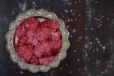 Beyinler, loş ışık altında siyah desenli yüzeyde tuz taneleriyle çevrili süslü metal plakalara yerleştirilmiş. Ürkütücü yemek tasarımı ve deneysel ayarlarıyla Cadılar Bayramı aşçılık atmosferi.