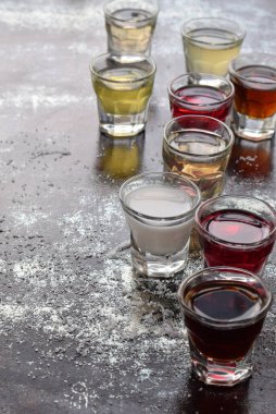 Kırsal desenli yüzeyde şeffaf bardaklarda servis edilen çok renkli alkollü içecekler. Parti etkinliği kavramı, bar kültürü, şenlikli kutlama, tatma deneyimi, çeşitli ruhlar, içki seçimi..