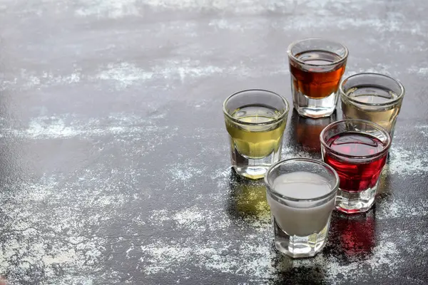 Yansıtıcı kırsal yüzeye yerleştirilmiş şeffaf bardaklarda farklı alkol çekimleri. Parti içeceği seçimi, sosyal toplantı, kutlama, renkli içecek sunumu, bar kültürü kavramı.