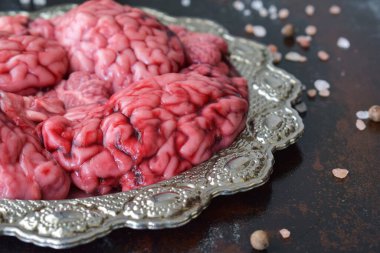 Mutfak yüzeyine tuz serpiştirilmiş gümüş süslü tabakta servis edilen ayrıntılı sığır beyni. Soğuk ışık ve korku tablosu ile Cadılar Bayramı temalı yemek konsepti.