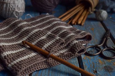 Yünlü iplikler, yumuşak tekstil ve mavi ahşap arka planda DIY aksesuarları. Doğal malzemeler ve el yapımı hislerle rahat bir çalışma sahnesi. Rustik örgü kompozisyonu