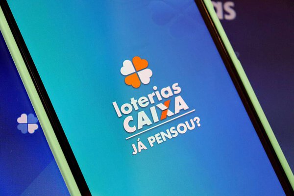 Bahia, Brazil - August 29, 2025: Loterias Caixa logo on smartphone screen on top of laptop. Brazilian Lottery concept.