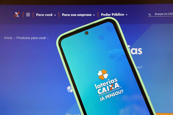 Bahia, Brazil - August 29, 2025: Loterias Caixa logo on smartphone screen on top of laptop. Brazilian Lottery concept.