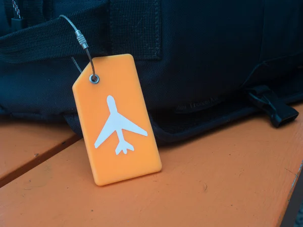A striking orange luggage label with a white plane logo is attached to a black piece of luggage.Security tag.Travel