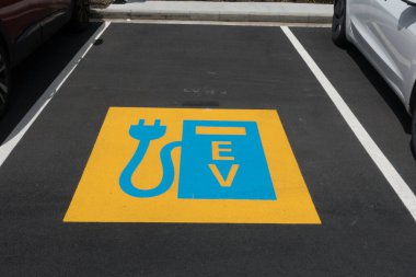 A blue and yellow sign on the tarmac of a parking bay indicates that it is an electric vehicle charging point. clipart