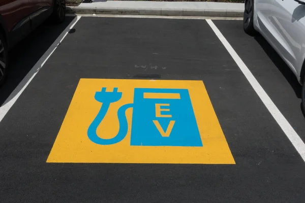 A blue and yellow sign on the tarmac of a parking bay indicates that it is an electric vehicle charging point.