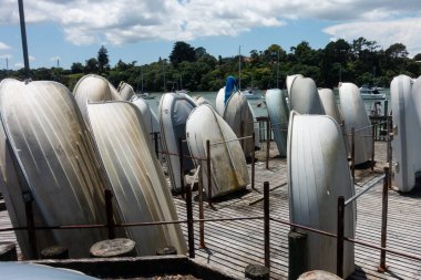 Several rowing boats are stood upright in a storage area on wooden decking.An estuary with other boats is visble in background
