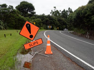 A roadside sign says slips a warning that landslides may be ahead.Orange Road sign with black exclamation mark