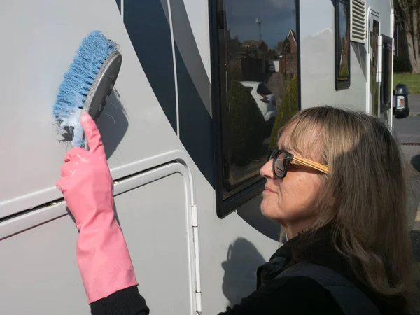 stock image An attractive lady hand cleans her motorhome recreational vehicle with a blue brush.She wears pink rubber gloves and sunglasses.Happy.