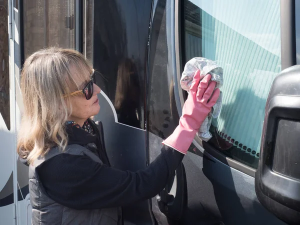 Stock image An attractive lady uses a cloth to wipe the side window of her motorhome recreational vehicle.She wears pink rubber gloves and sunglasses