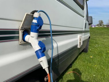 İki elektrik bağlantı kablosunun bir prizden çalışmasını sağlayan bir dağıtıcı konnektörü, bir karavan eğlence aracının yan tarafında görülebilir