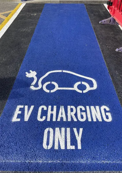 A painted sign on tarmac surface  indicates an EV charging point for electric vehicles.Blue background with white lettering.Ecological.Vertical image
