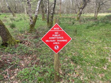 Tahta bir korulukta beyaz harfli kırmızı elmas işareti 'Savunma Bakanlığı giremez. Askeri Eğitim Bölgesi' diyor..