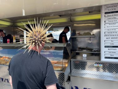 Crick-UK-26 Mayıs 2024 - Sarı dikenli punk tarzı saçı olan bir adam fast food dükkanında duruyor.