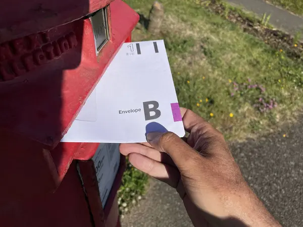 stock image A hand puts an envelope for the United Kingdom General Election postal vote in a red post box.First Class.Enveloppe B