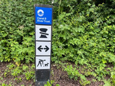 Crick-Northampton-UK- May 23,2024- Signs and Symbols on a marker post on a canal towpath has symbols indicating various restrictions and instructions for narrowboat users.Canal and River Trust.Hedge in background clipart