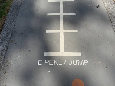 Bir oyun parkının asfaltındaki işaretlerde 'E Pike' ve 'Jump' kelimeleri var. Maori ve İngiliz Dili. Yeni Zelanda