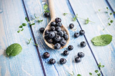 Fresh juicy blueberries with green leaves on a blue background. Healthy berry, organic food, vitamin, blue food.