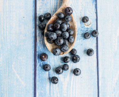 Fresh juicy blueberries with green leaves on a blue background. Healthy berry, organic food, vitamin, blue food.