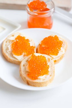 Slices of bread with red caviar on a plate, on a white background.