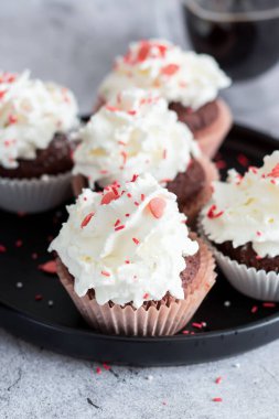 Coffee with muffins, muffins with cream and sprinkles. On a concrete background