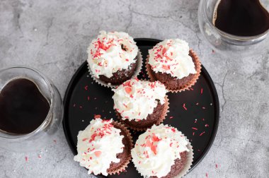 Coffee with muffins, muffins with cream and sprinkles. On a concrete background